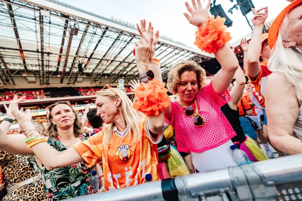 Feestende bezoekers in oranje outfits bij de dranghekken